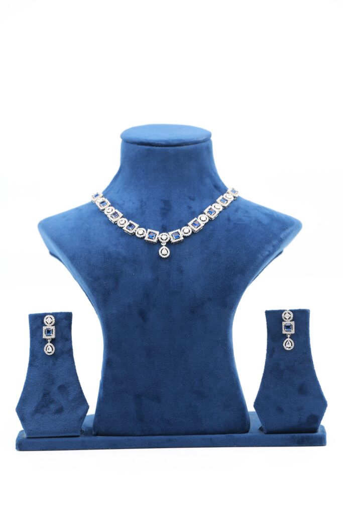 Square-cut sapphire-blue stones framed in brilliant-cut halos with a single-drop pendant. Matching earrings echo geometric elegance.