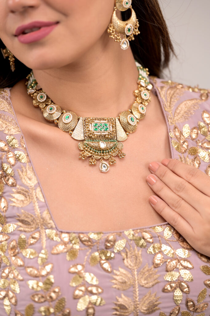 Mahek Heritage Set featuring an antique gold-tone choker necklace with textured hammered panels and green stone detailing, paired with matching chandelier earrings with beaded drops. Antique gold choker set, Indian heritage jewellery, traditional bridal necklace, hammered texture jewellery, festive ethnic jewellery set